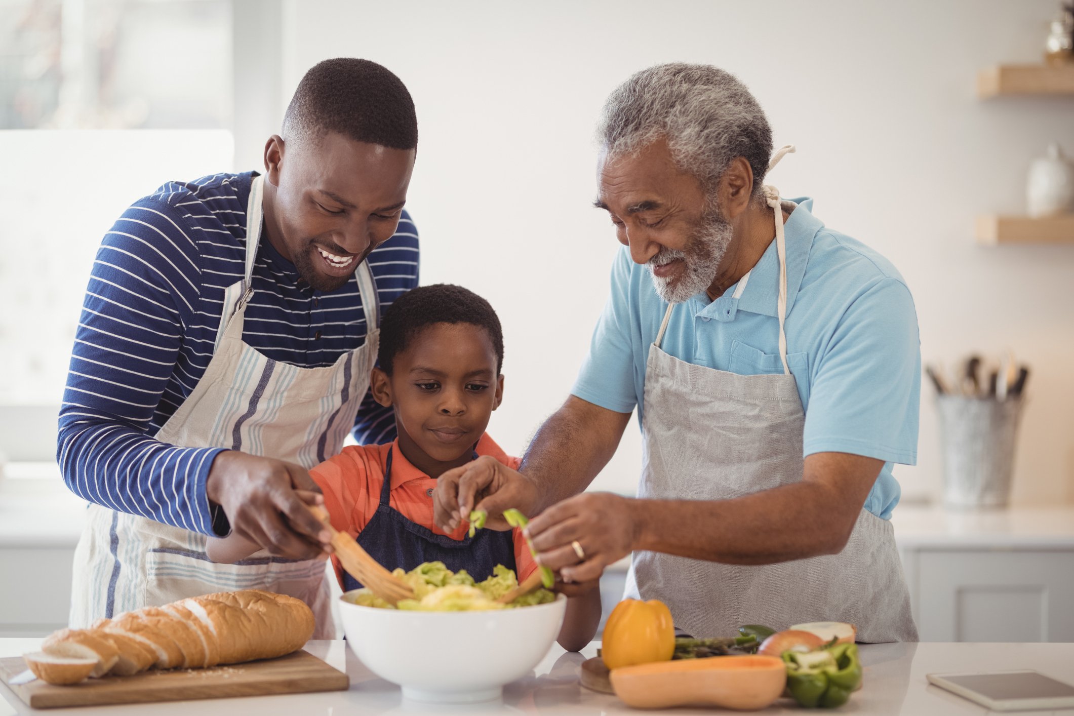 Younger man, older man and child prepare meal in kitchen.