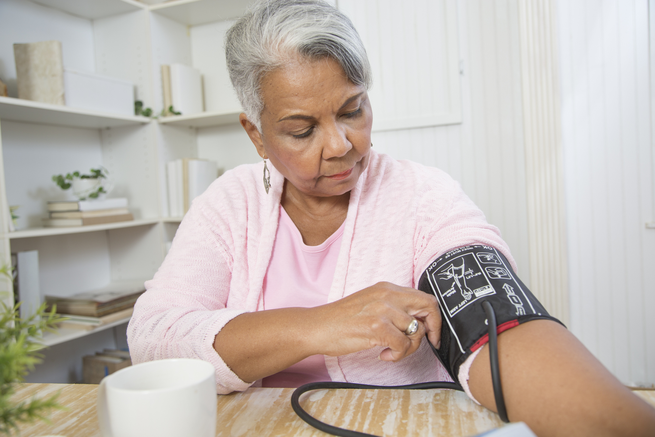 Woman at kitchen table adjusts blood-pressure cuff.