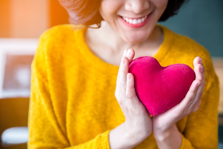 Woman in yellow sweater holding magenta heart pillow